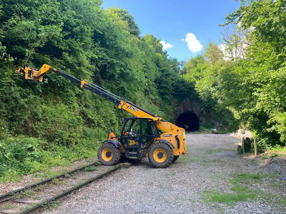 JCB telehandler with tree shears clearing vegetation by a railway tunnel at Great Elm, Somerset